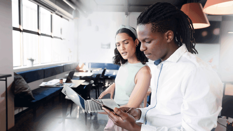 Multiracial young businessman and businesswoman with laptop and smart phone discussing in office