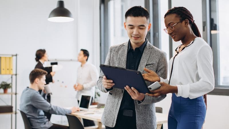 African businesswoman and Asian businessman using a tablet with interracial group of business men & women team
