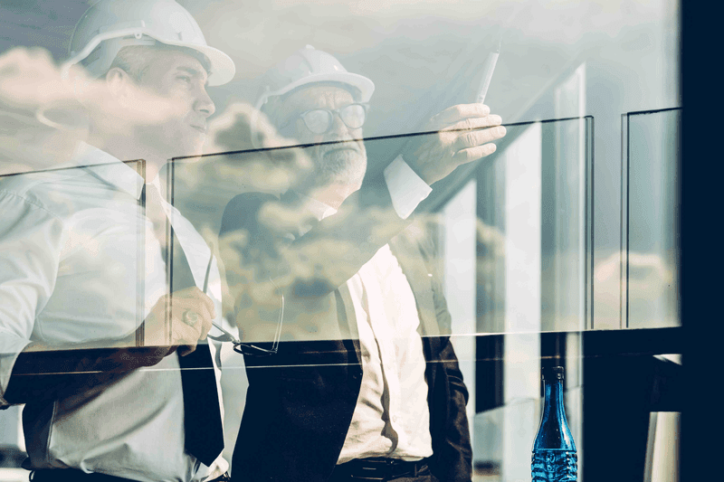 Two industrial engineer wear safety helmet engineering working and talking with drawings inspection modern city background. Industry, Engineering, construction concept. With copy space for your text.