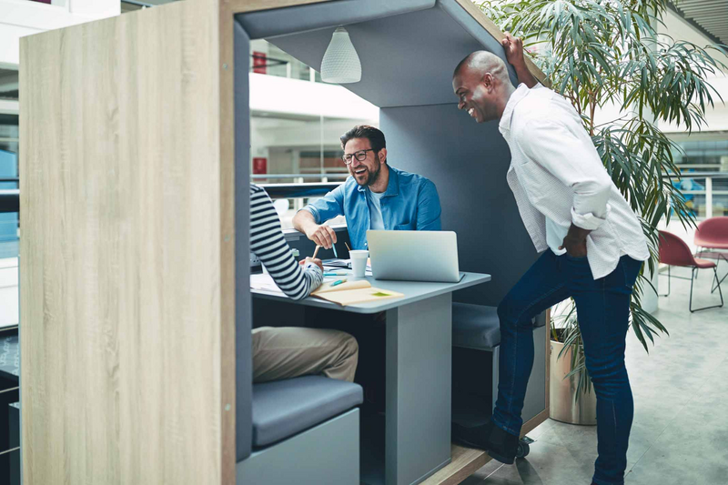 Diverse businessmen laughing together in an office meeting pod