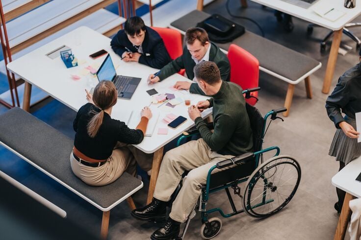 Web_Mobile-Business team meeting with diverse colleagues including a man in a wheelchair collaborating at a table