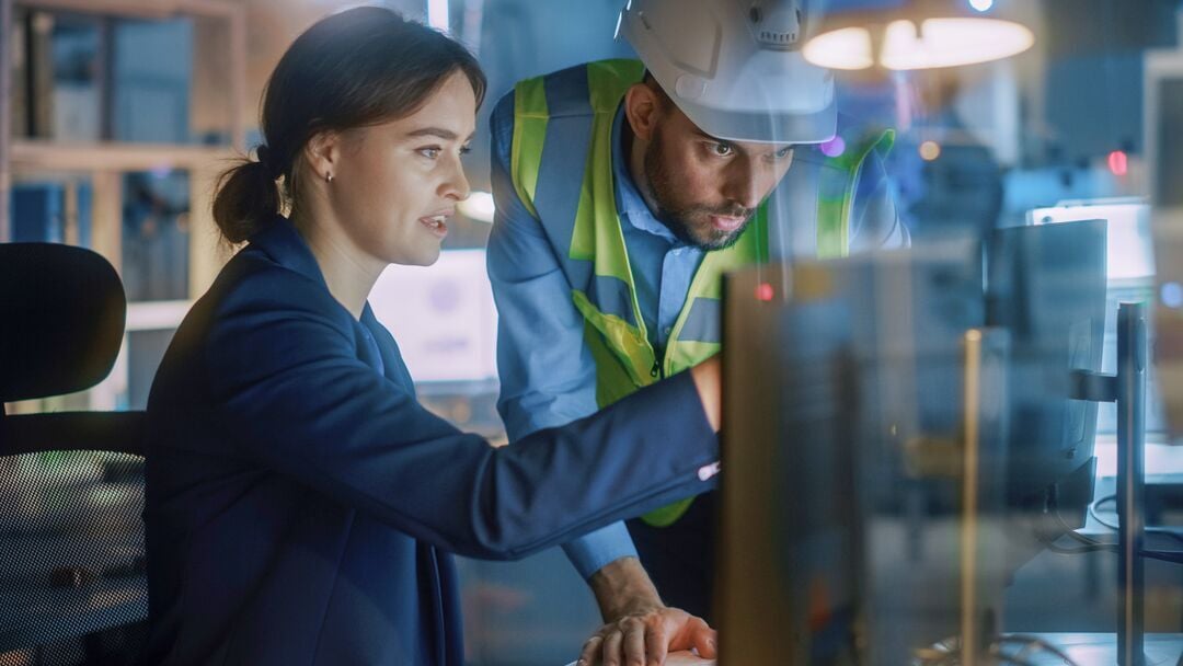 Web_Desktop-Modern Factory Office_ Male Project Manager Talks to a Female Industrial Engineer who Works on Computer. Professional Teamwork, Specialists Solving Problems, Finding Solutions